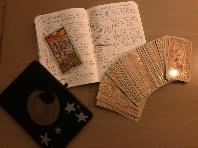 A witches grimore and tarot deck are open on a table