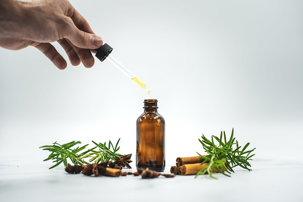 Image of a hand pulling some essential oil from a jar surrounding by cinnamon and thyme containing the essential oil