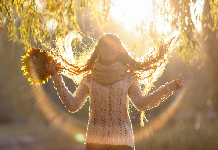 Woman walking through tress hol
ding leaves basking in the autumn sunshine