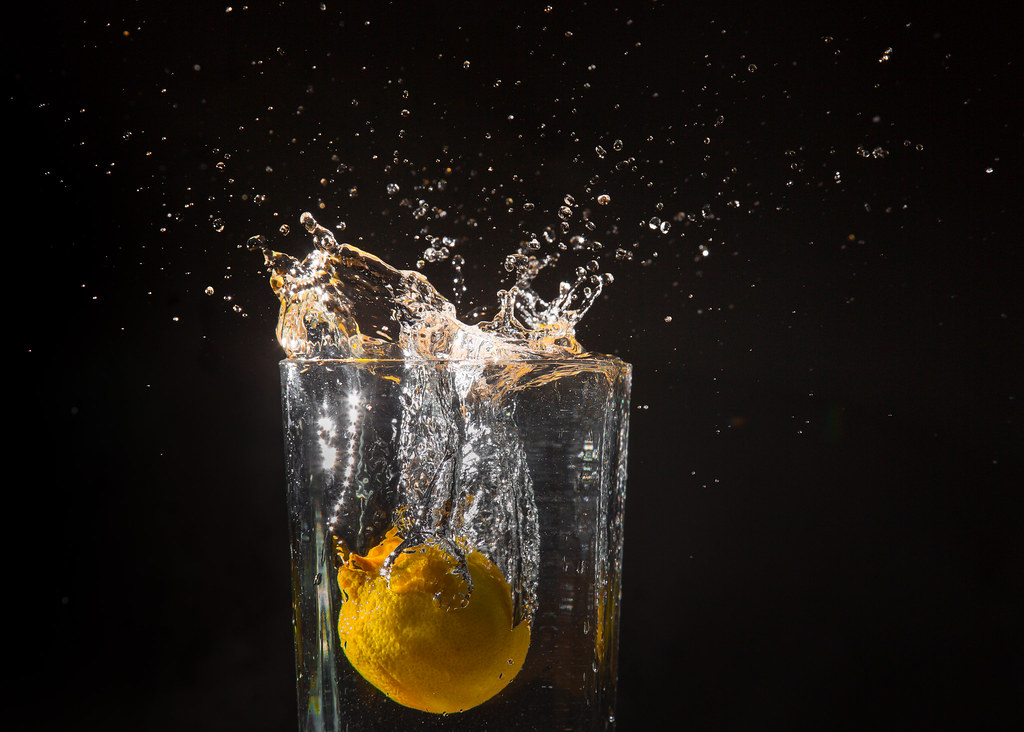 A lemon being dropped intoa glass of water and making a slash against a black back ground 